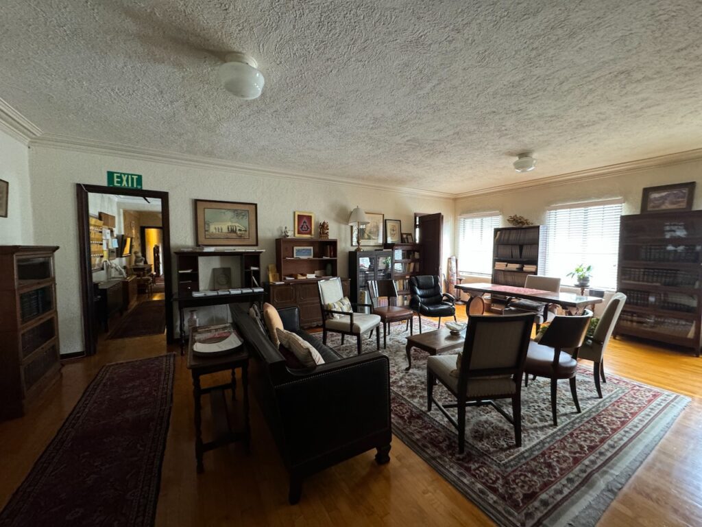 Cozy meeting room at Theosophy Hall with upholstered chairs and sofas arranged around a central coffee table, flanked by bookcases and a large area rug.